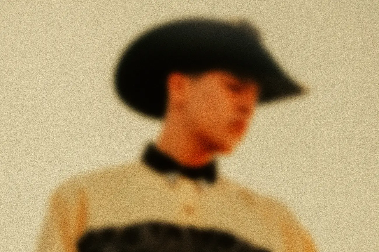 A blurred photo of a young man in a cowboy hat
